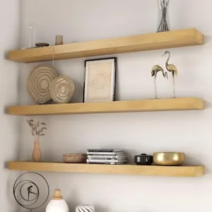 Three thick white oak floating shelves displaying books, framed art, and pottery.