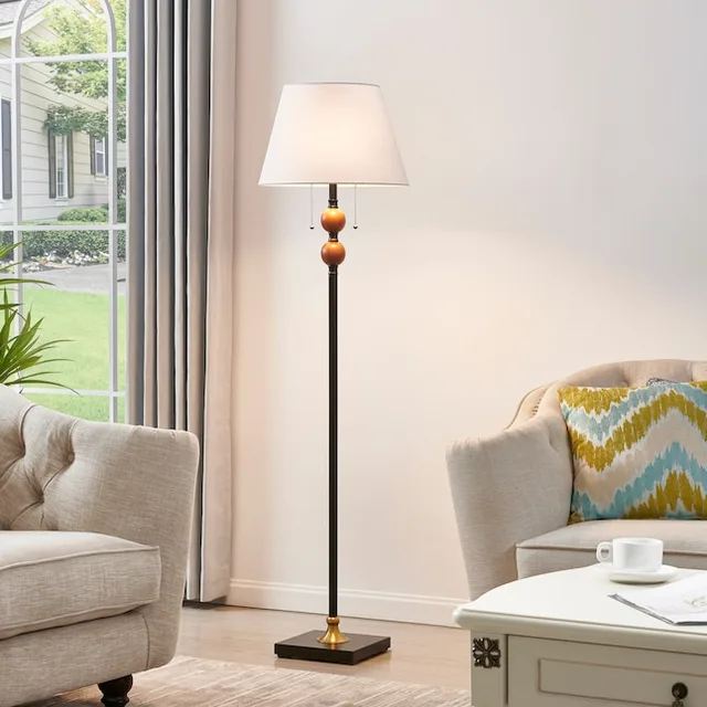 Black and gold floor lamp with a white fabric shade beside an armchair.