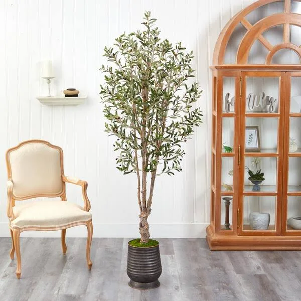 Artificial olive tree in a ribbed metal planter beside a wood-framed mirror.