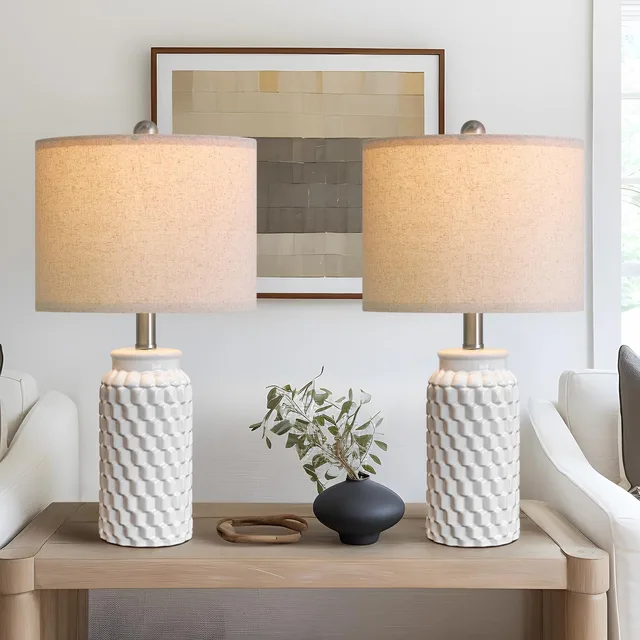 Two white textured ceramic table lamps with beige shades on a console.