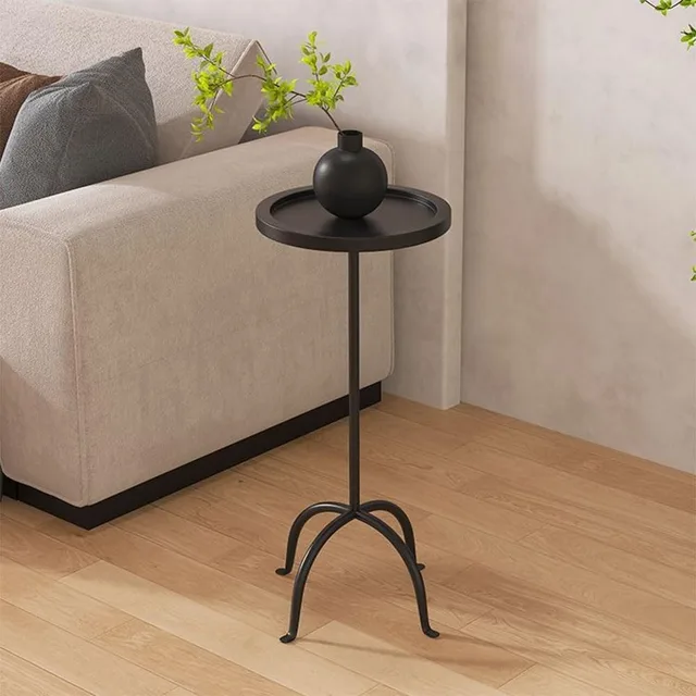 Small black round pedestal table with curved feet beside a sofa.